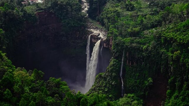 Aerial drone video of hidden waterfall in the tropical forest of East Java, Indonesia, Lush green jungle surrounds the tall waterfall as it flows powerfully down rocky cliffs. 
