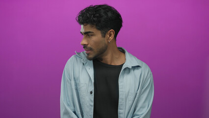 Young hispanic man wearing denim shirt tilts head and closes eyes in a purple studio setting;...
