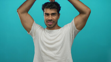 Man arm raises forming heart gesture in bright turquoise studio with fingertips touching overhead;...