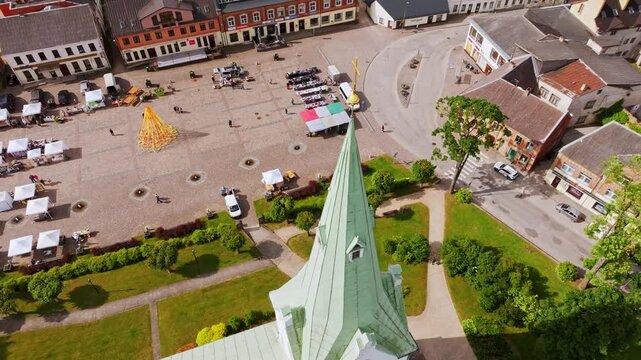 Drone dives close to green church spire and reveals Dobele's vibrant old square