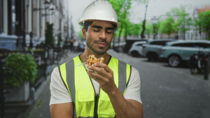 Man eating golden waffle on busy urban street wearing yellow vest and engineer hardhat;...