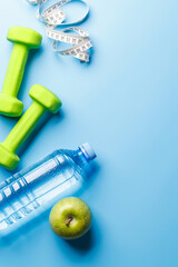 Flat lay of dumbbells, water bottle, and green apple over a bright blue