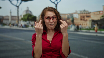 Fototapeta premium Woman in red shirt making expressive gestures on urban street with historical buildings, demonstrating an emotional reaction outdoors in a city setting