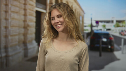 Woman hair flows as smiling face brightens street scene where blonde young subject poses in outdoor...