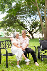 smiling senior couple embracing and holding hands while resting on wooden bench in park with ...