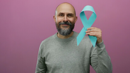 Man with beard holding blue awareness ribbon against isolated pink background confidently posing for health campaign support.
