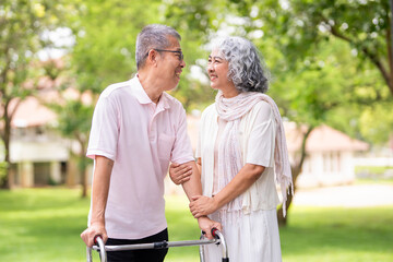 Happy loving Asian senior couple taking a walk with walker in the park.