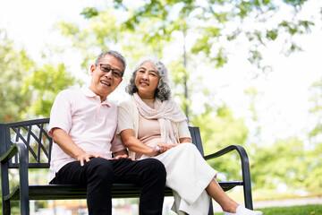Senior couple sitting on a bench in the park smiling and looking at camera.