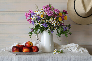 Summer still life with wildflowers in a white jug and peaches on a table