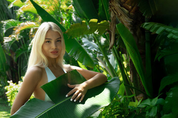 Woman stands in a tropical garden, holding a leaf
