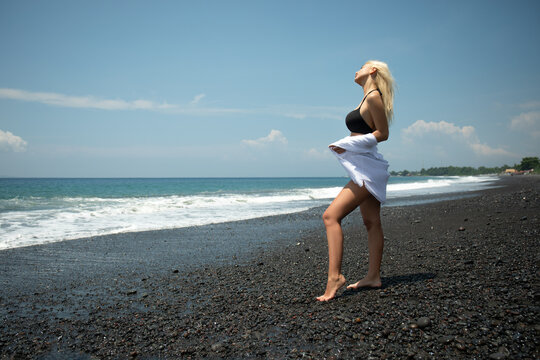 Woman stands on black sand beach enjoying the warm sun