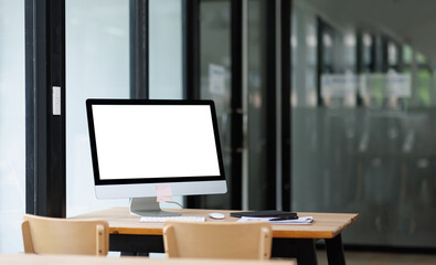 Open desktop with blank screen view of a white-screen desktop computer mockup and accessories on a wooden desk in a workplace office room. private office, office workspace.

