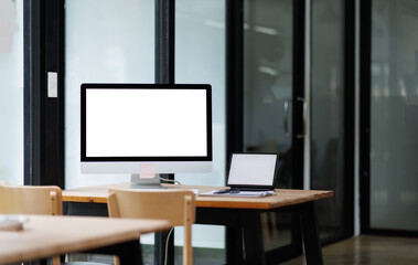 Open desktop with blank screen view of a white-screen desktop computer mockup and accessories on a wooden desk in a workplace office room. private office, office workspace.
