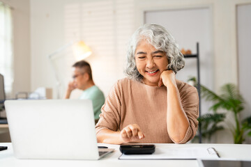 Happy senior couple using laptop counting taxes refund receipts to save money at home. Old man and...