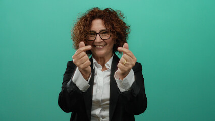 Woman smiling with curly hair against a green background, wearing glasses and a suit, expressing...