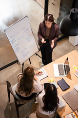 Confident mature business professional woman talking to younger female colleague at office table,...