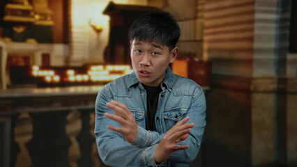 Young man gesturing passionately indoors, set against a serene church background, suggesting an intense discussion or sermon taking place.