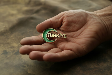 Elegant gold 'Türkiye' emblem with crescent rests gently in open palm, symbolizing pride and heritage.