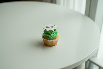 Delightful green frosted cupcake with a "Sweet" star topper sits on a bright white table, perfect for celebrations and baking themes.