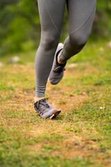 Woman in sportswear spraining ankle while running outdoors, vertical close-up of foot twisting on uneven grass surface in nature, risk of sports injury and leg trauma during outdoor activity