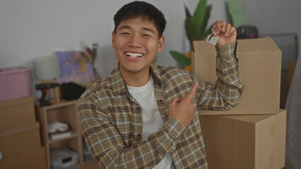 Young man smiling and holding keys in a new home surrounded by moving boxes, symbolizing a fresh start in a modern apartment living room.