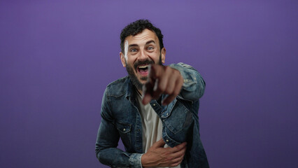 Happy hispanic man with a beard laughing in front of a purple background wearing a denim jacket,...