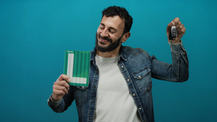 Hispanic man with beard holding car keys and learner sign confidently against blue background.