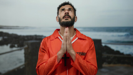 Man in orange jumpsuit praying on a beach with ocean waves hitting the shore in the background...
