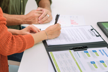 Asian couple reviewing and sign contract financial documents with the guidance of  advisor at...