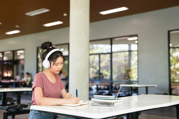 college student in casual clothes with wireless headphone doing home work spend time in canteen...