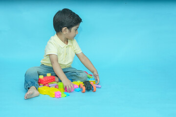 Indian child boy playing with educational toys isolated against blue background. 2-3 year playful kid having fun while sitting on the floor, Childhood. Copy space