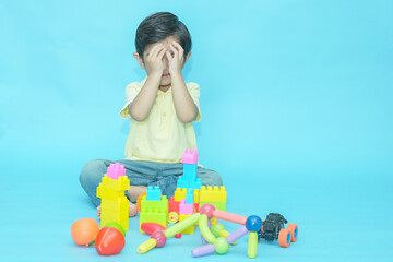 Indian baby boy child playing with educational toys isolated against blue background. 2-3 year playful kid having fun while sitting on the floor, Childhood. Copy space