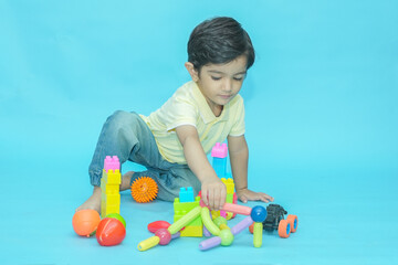 Indian child boy playing with educational toys isolated against blue background. 2-3 year playful...