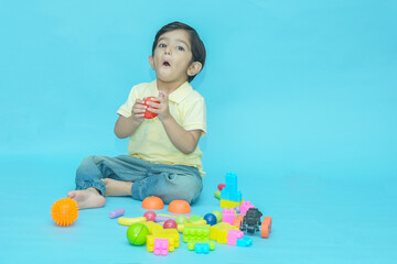 Indian child boy playing with educational toys isolated against blue background. 2-3 year playful kid having fun while sitting on the floor, Childhood. Copy space