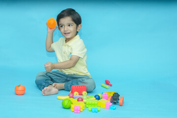 Indian child boy playing with educational toys isolated against blue background. 2-3 year playful kid having fun while sitting on the floor, Childhood. Copy space