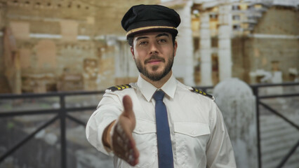 Young man in uniform extending handshake outdoors against architectural background during sunny day