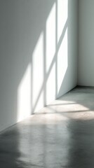 Obraz premium Empty corner of white room with soft daylight and shadow cast from large window ideal for minimal interior design visuals, architectural photography and peaceful atmosphere compositions