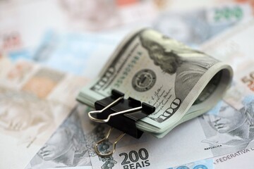 Bunch of US dollar bills lies on big amount of Brazilian reais banknotes close up