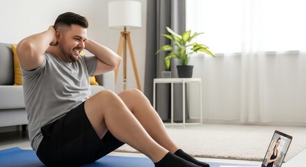 A plus-size man smiling through the effort as he does sit-ups on a mat in his living room, following a virtual trainer on a laptop.