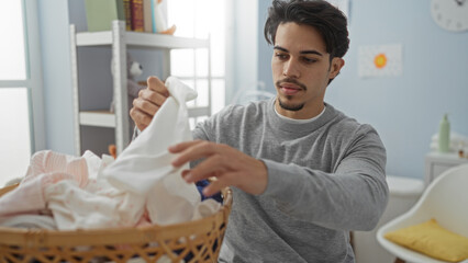 Young hispanic man doing laundry in a home interior, focused on task, sorting clothes in a bright and tidy environment.