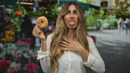 Young woman holds donut by hand at outdoor flower market with a disgusted frown; disgust reluctance.