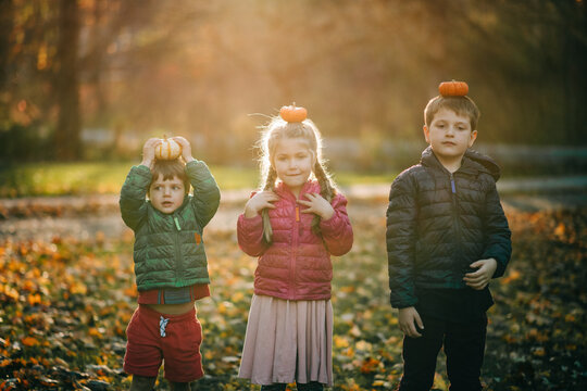 Children balancing pumpkins on their heads in autumn park