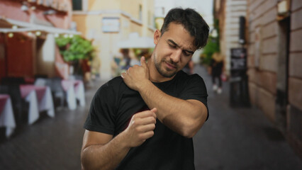 Fototapeta premium Young man expressing discomfort on a bustling city street, surrounded by blurred urban scenery, capturing a moment of outdoor pain and interaction.