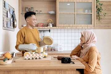 Asian cheerful couple enjoying their time cooking and sharing moments in a cozy wooden kitchen with...