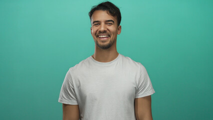 Young hispanic man smiling confidently against vibrant green background wearing casual white shirt...