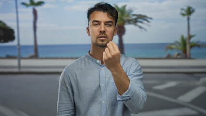 Young hispanic man gesturing in frustration on seaside promenade with palm trees in the background,...