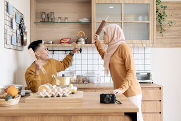 A joyful couple using kitchen utensils in a humorous manner while cooking together, depicting fun...