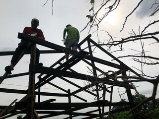 Silhouettes of carpenters on top of the wooden frame are joining girders and beams to construct a...