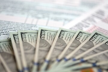 Big amount of United States USD dollar bills banknotes on table with 1040 tax return form