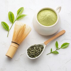 flatlay of a matcha tea set with bamboo whisk, matcha bowl, matcha powder in ceramic spoon, and green tea leaves on textured white surface